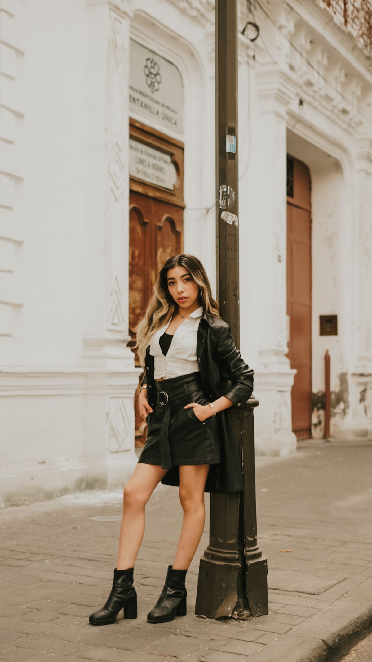 Latina woman in a black leather jacket over a fitted dress in the city