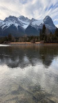 Breathtaking view of snowy Canadian Rockies reflected in a calm lake under a dynamic sky.