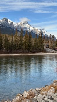 Breathtaking view of snow-capped Canadian Rockies with lake reflection and lush pine forest.