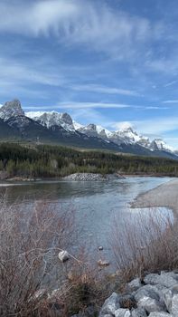 Snow-capped mountains and a tranquil river under a bright blue sky.