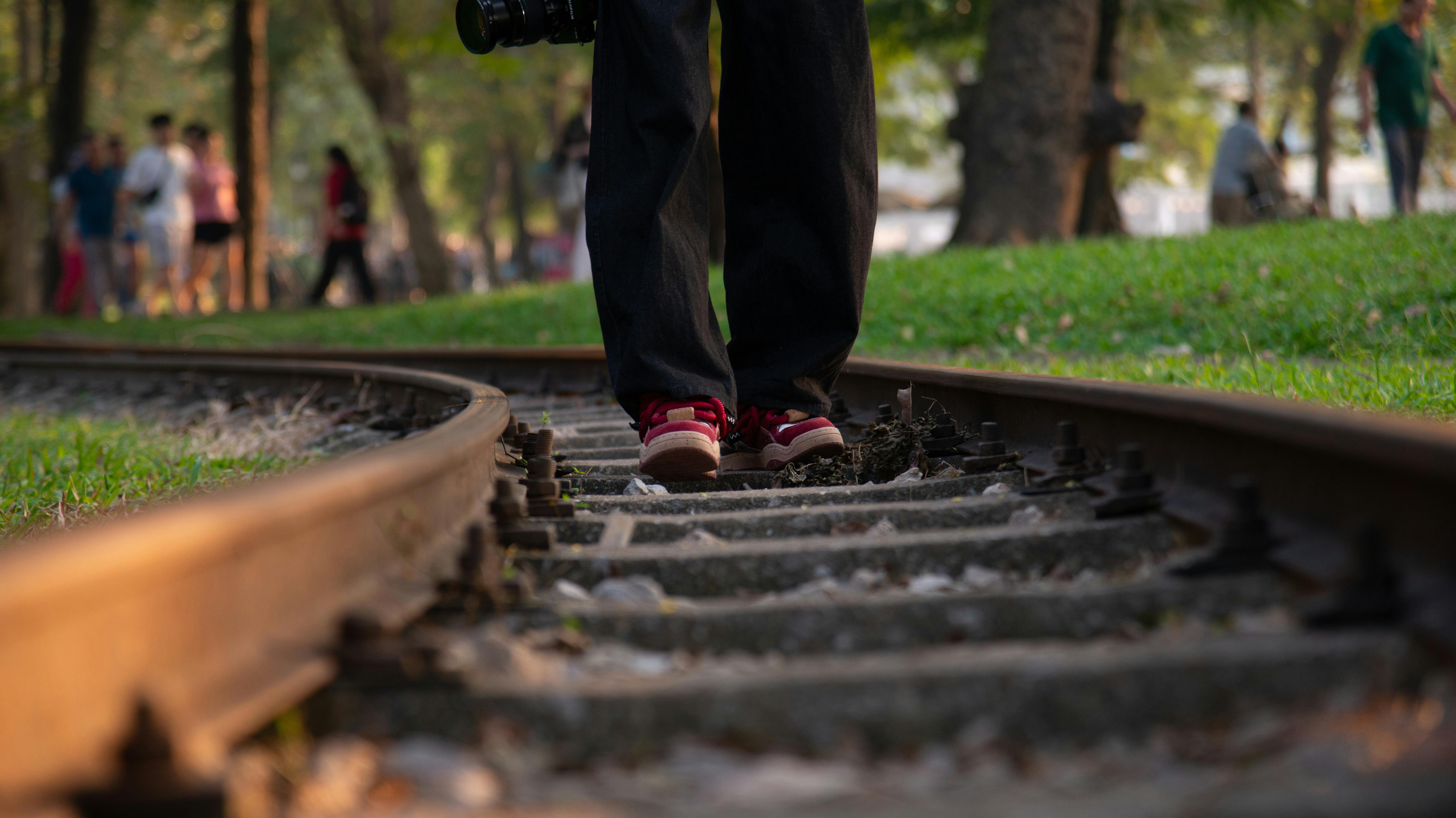 A person walking on a railroad track in a park with a soft focus background.