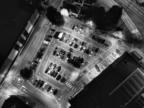 Free Black and white aerial view of a city parking lot at night with cars and streetlights. Stock Photo