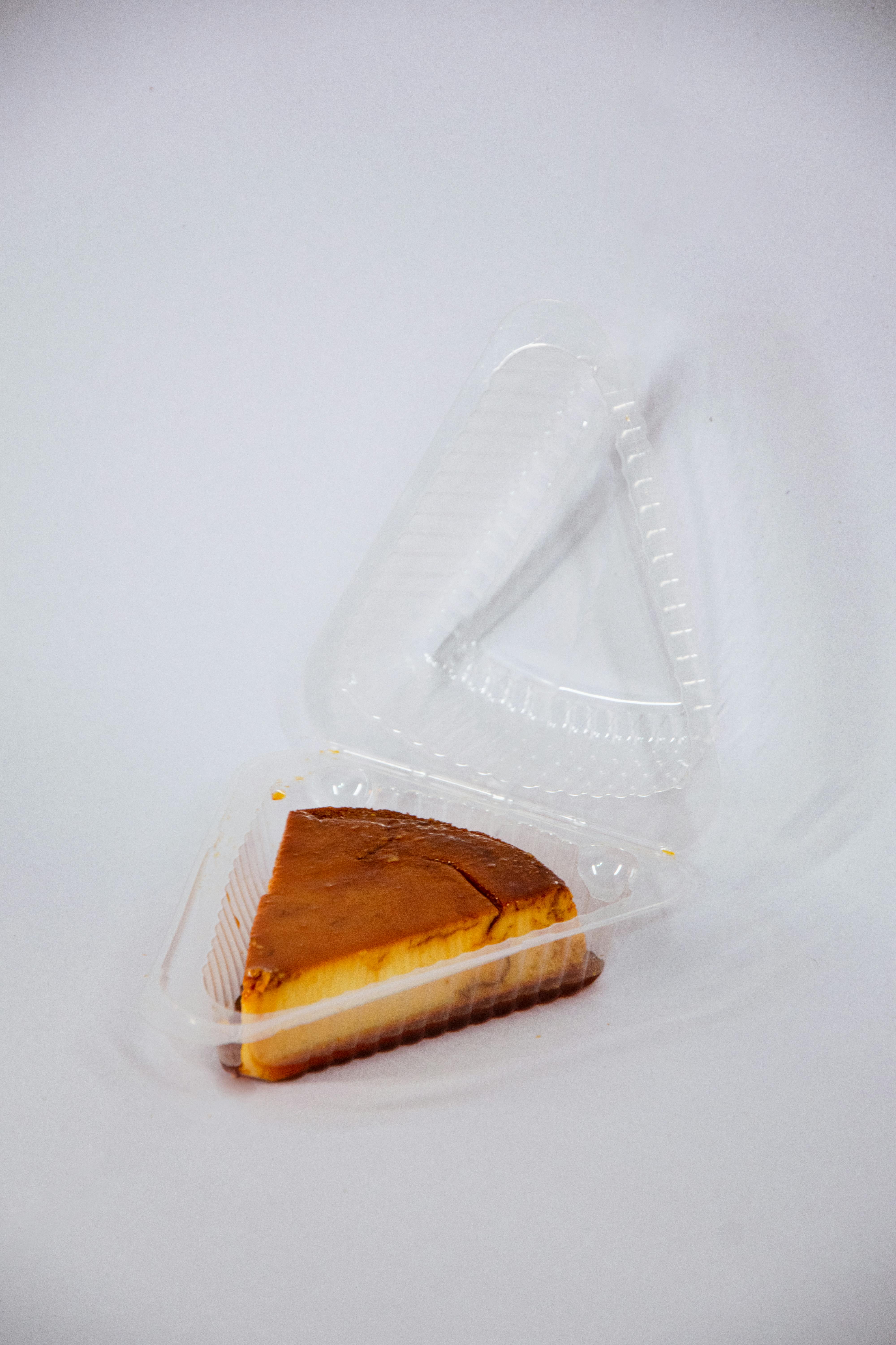Delicious cheesecake slice in a clear plastic takeout container, isolated on white background.