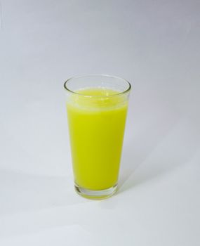 A vibrant yellow fruit juice in a clear glass, set against a white background.