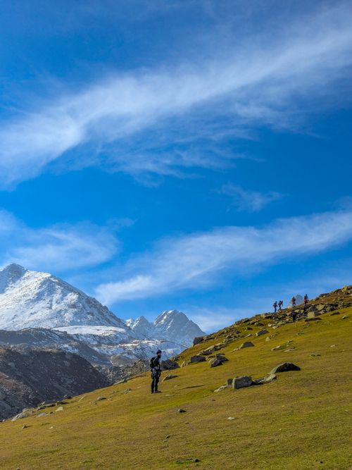 Free Photograph of hikers in a picturesque mountainous landscape with snow-capped peaks and clear blue skies. Stock Photo