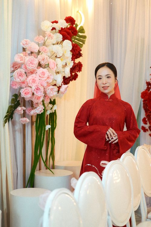 Free Asian woman in a red dress standing by floral arrangement at a formal indoor event. Stock Photo
