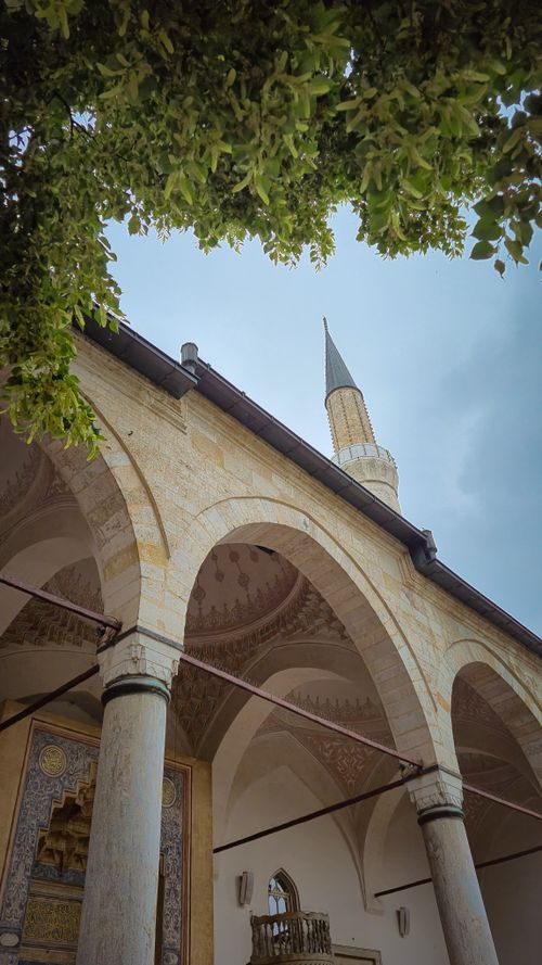 Free Stunning view of a mosque's arches and minaret with lush green foliage overhead. Stock Photo
