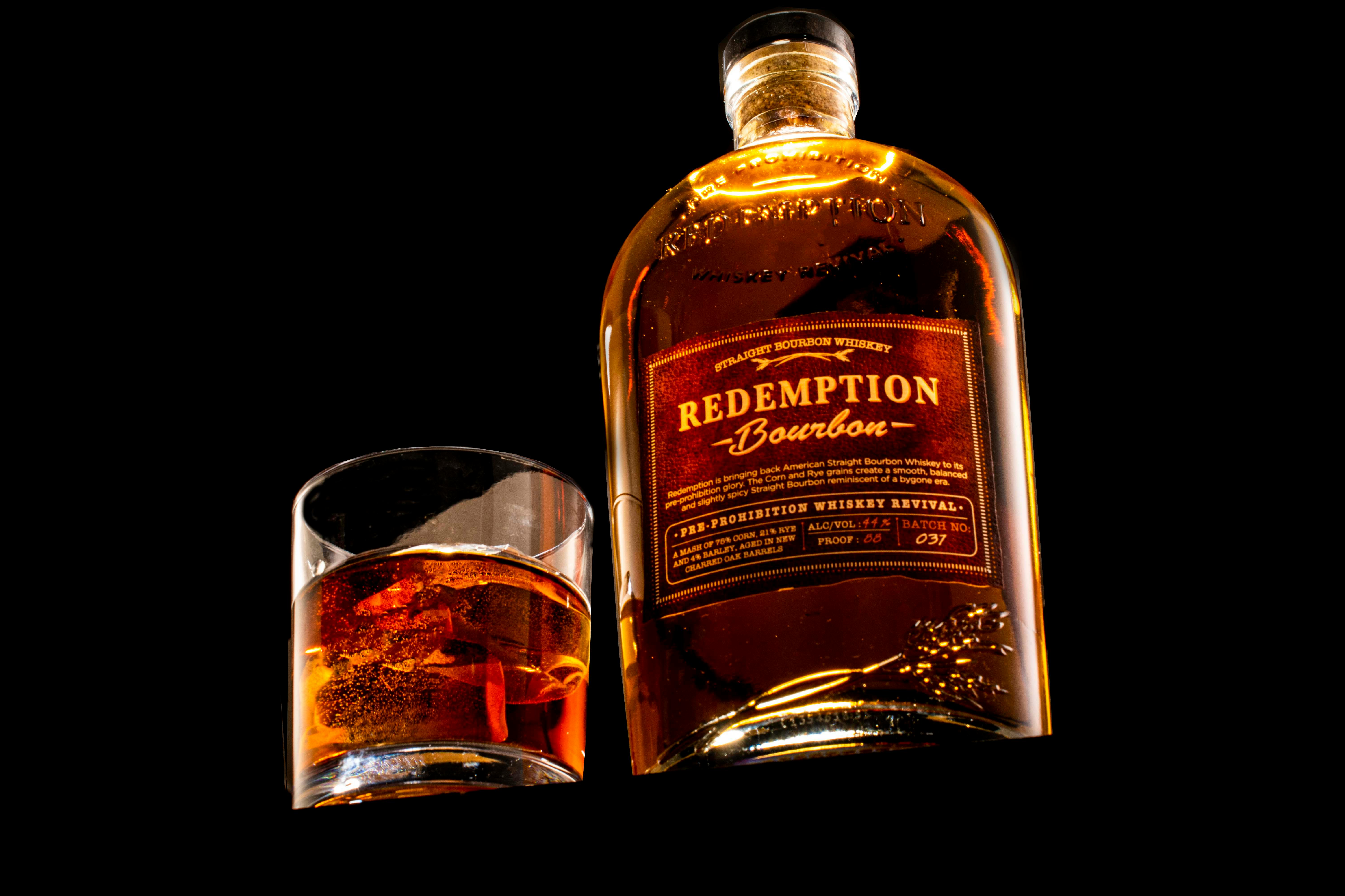 Close-up of Redemption Bourbon bottle with a glass of whiskey on black background.