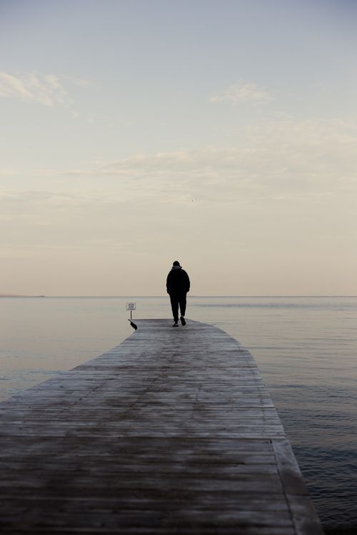 Free Lone person walking on a wooden pier extending into a calm sea at twilight. Stock Photo