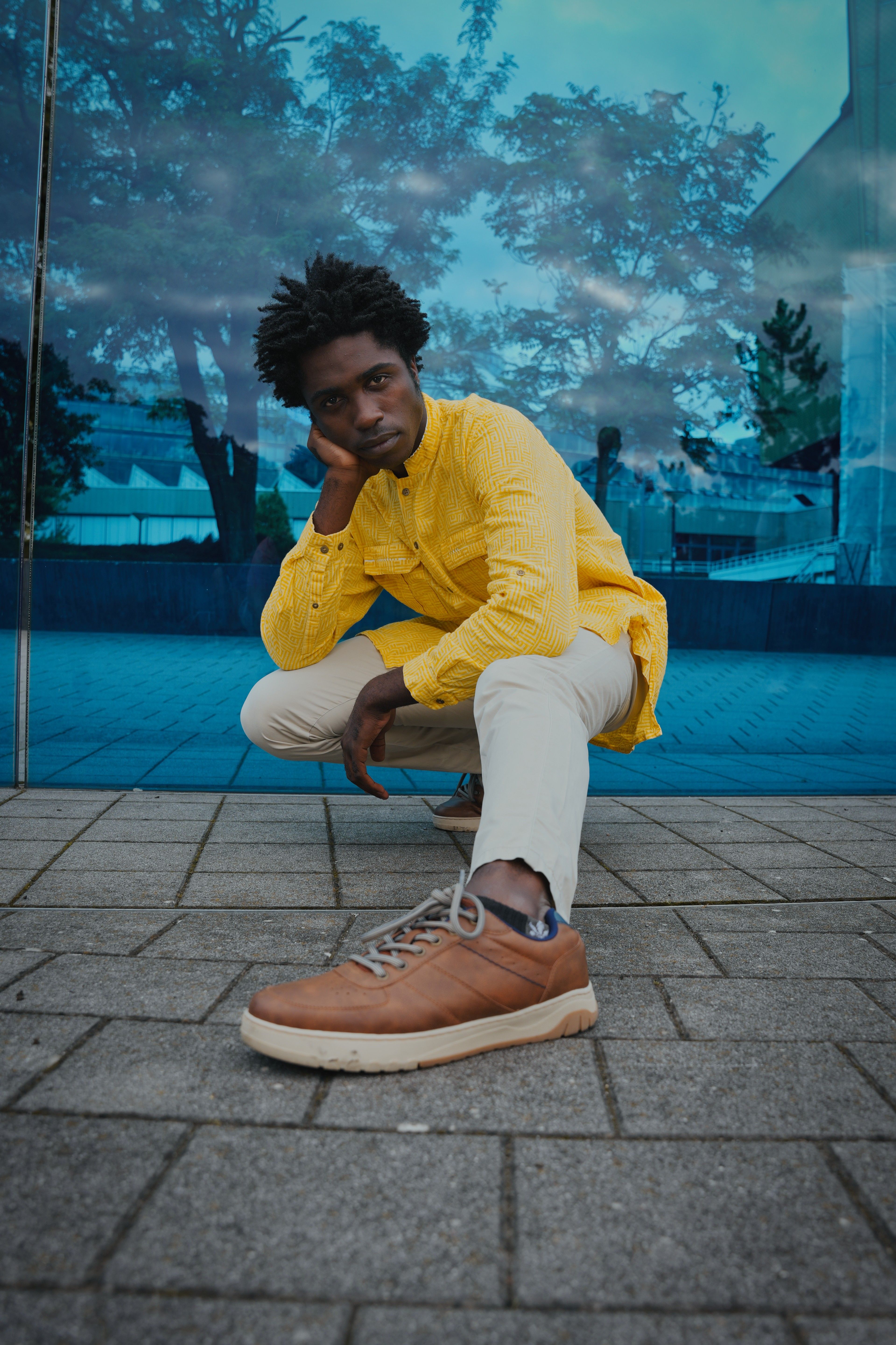 Confident young man in a yellow shirt posing against a blue glass wall in Berlin.