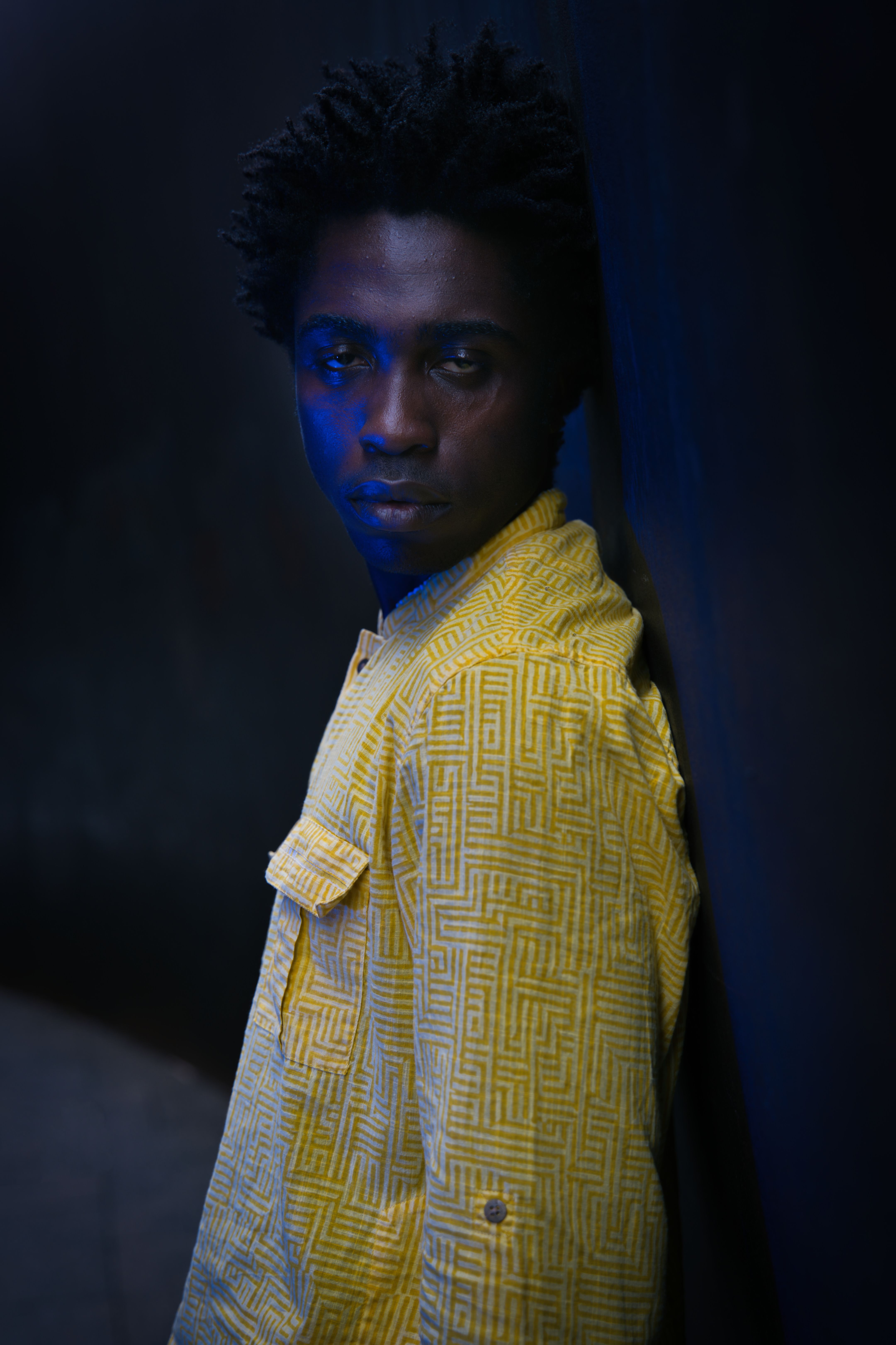 Moody portrait of a man in a yellow jacket under blue lighting.