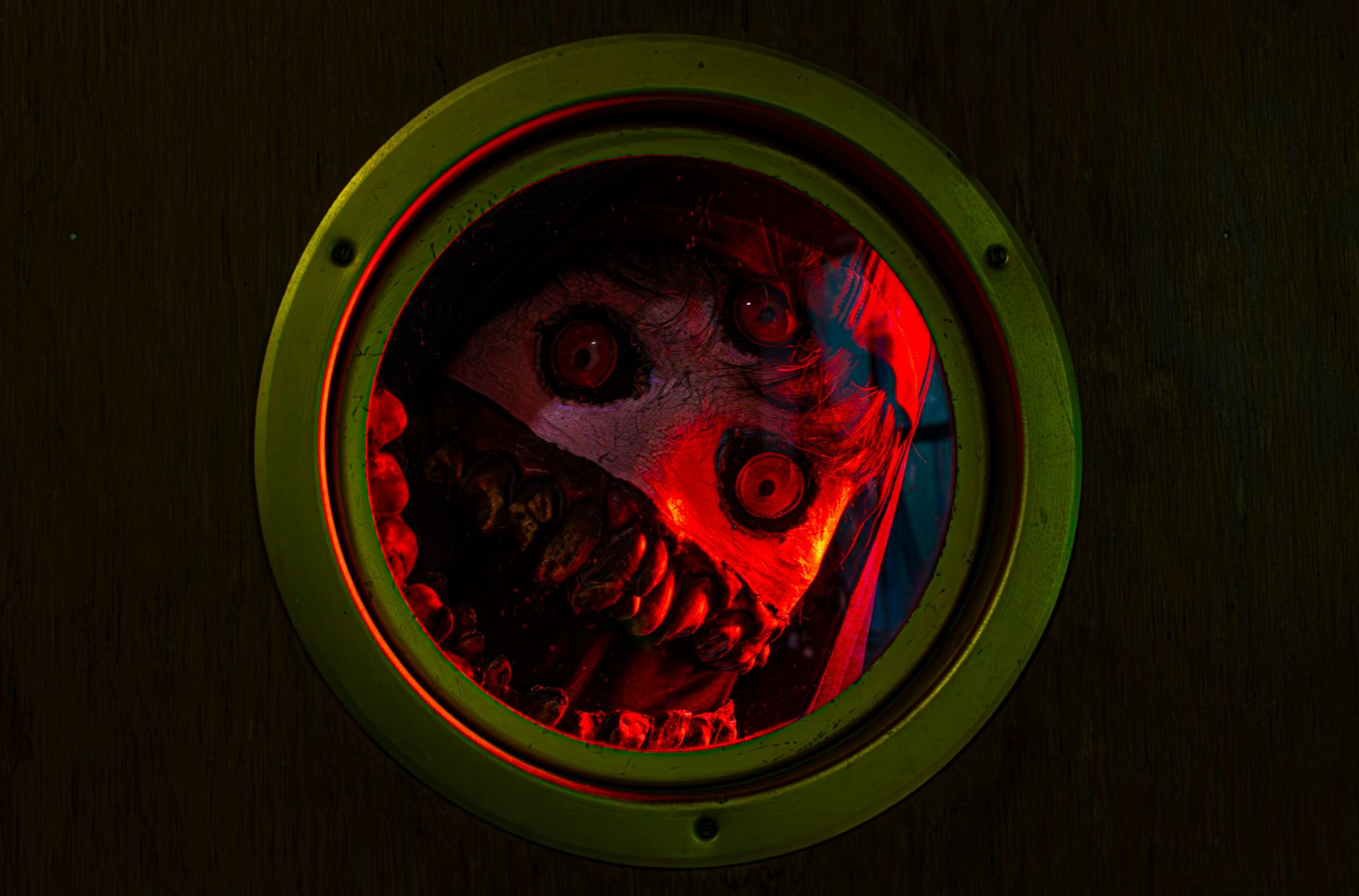 Eerie monster face peering through a porthole with red lighting, creating a spooky atmosphere.