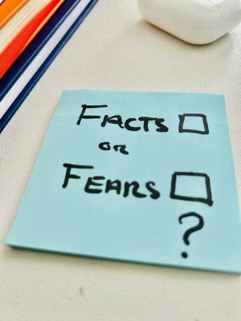 A blue sticky note asking "Facts or Fears" placed on a desk, prompting reflection.