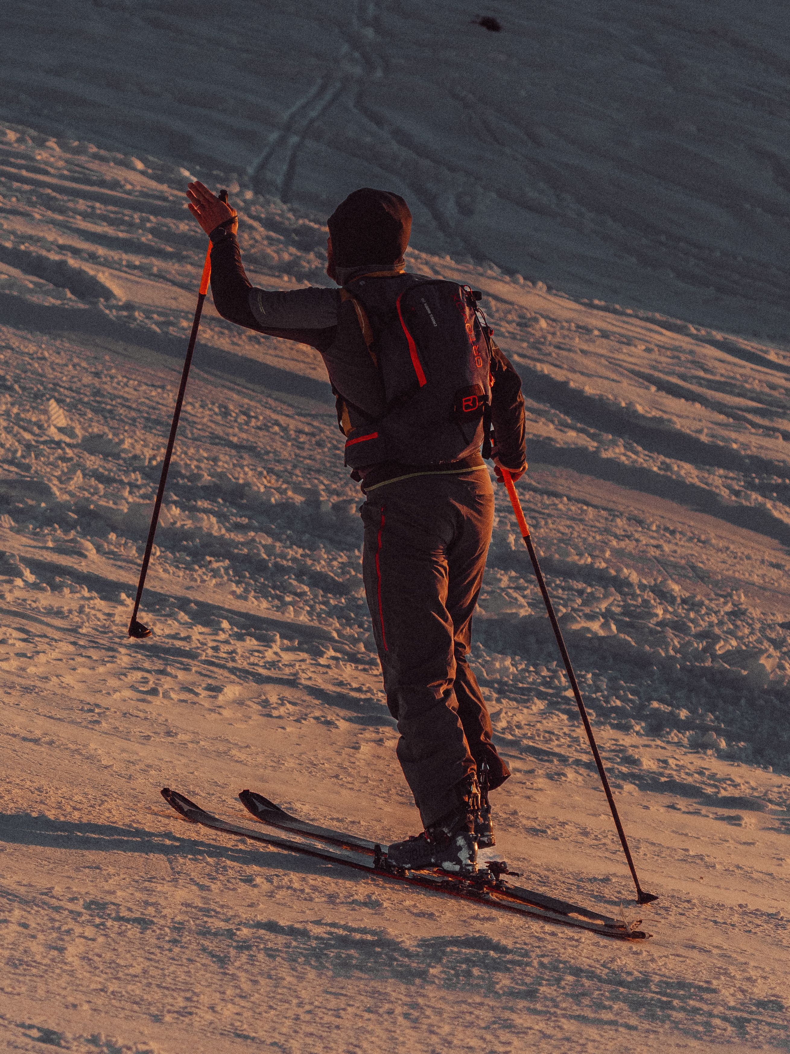 A skier climbs a snowy mountain slope during sunset, capturing the thrill of backcountry skiing.