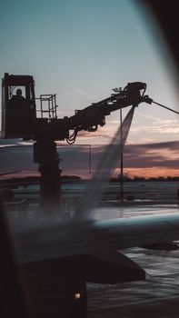 Silhouette of aircraft deicing at sunset, creating a dramatic airport scene.