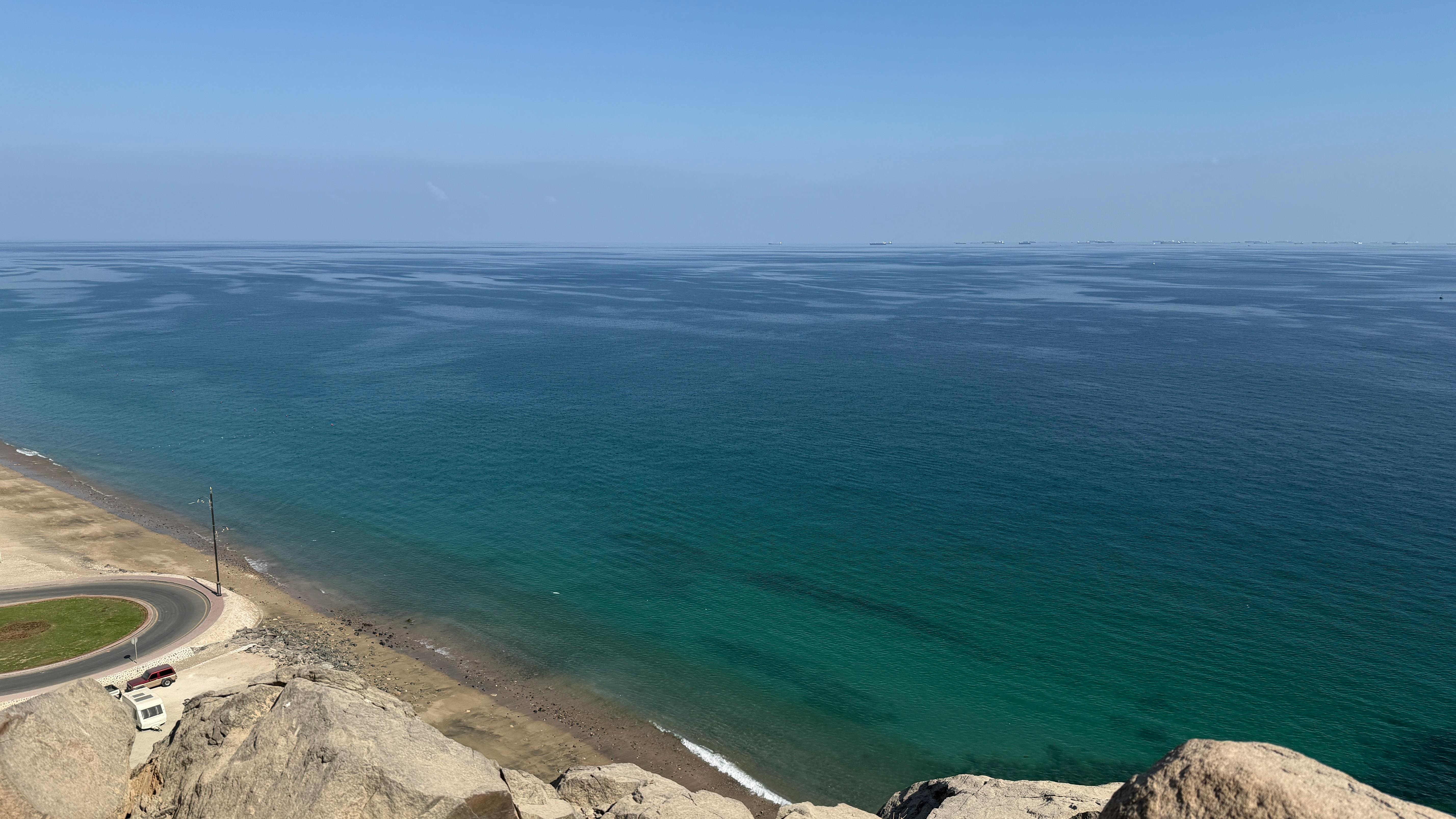 A breathtaking view of a coastal road meeting the clear blue ocean under a bright sky.