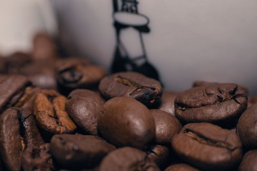 Macro shot of roasted coffee beans next to a cup, creating a warm and rich atmosphere.