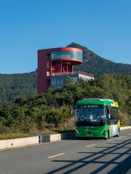 Photo by Da Na A vibrant city bus passing by a modern building with a mountain backdrop.