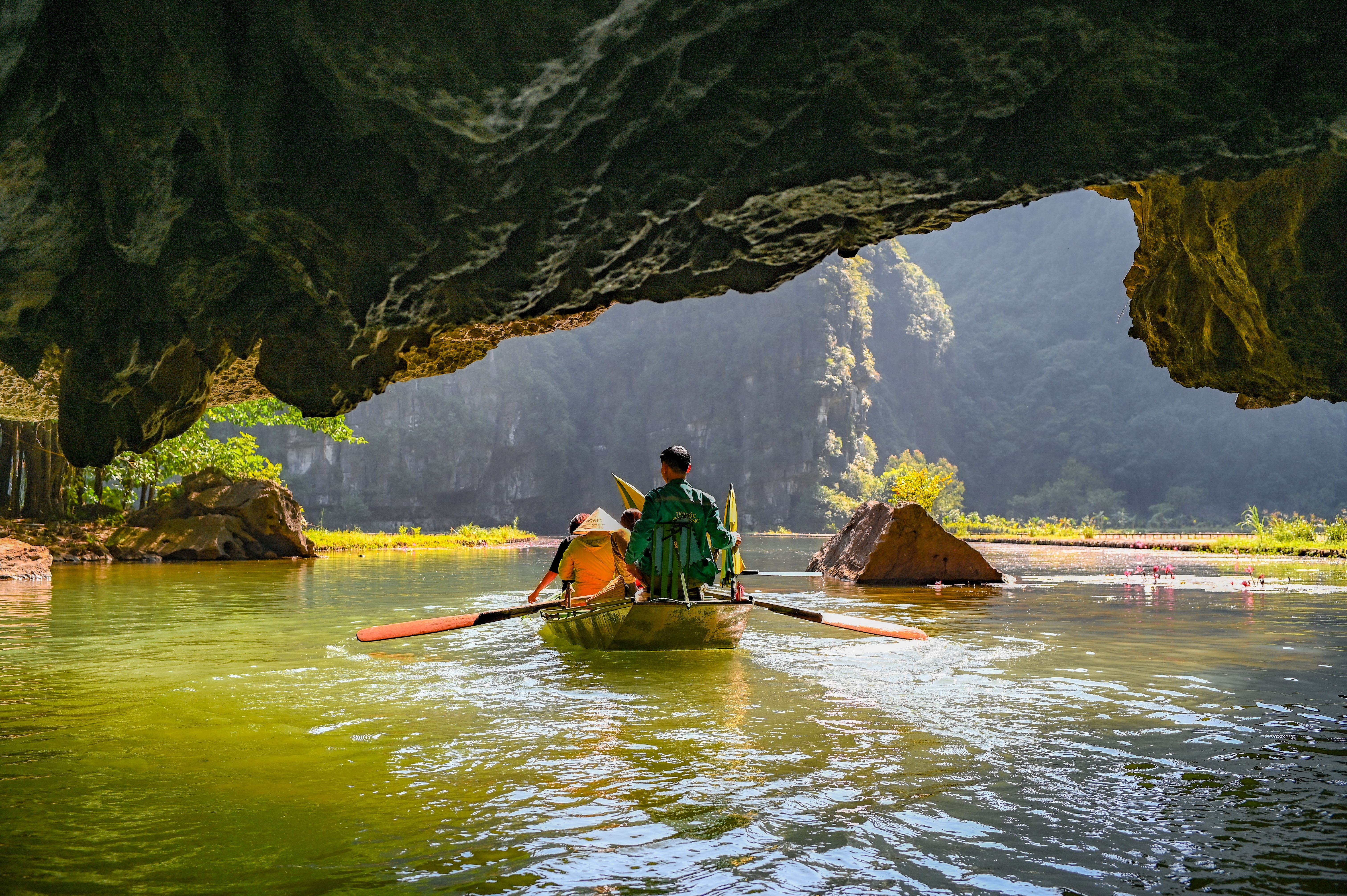 Two people kayaking through a scenic cave river surrounded by lush greenery and limestone formations.