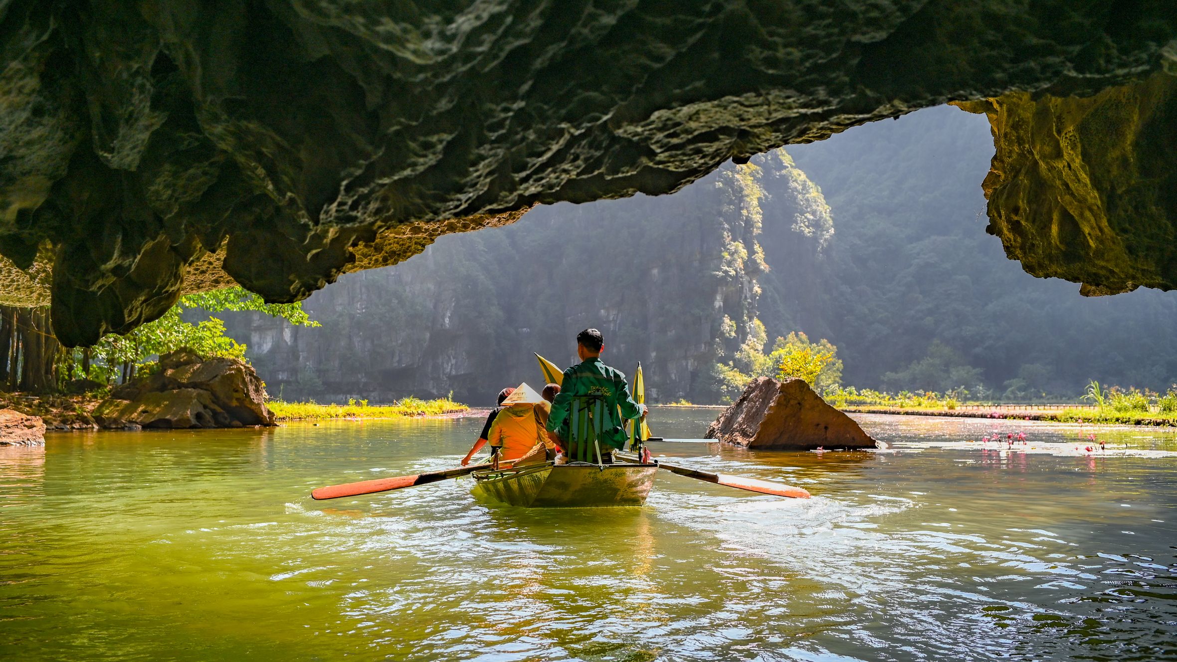 Two people kayaking through a scenic cave river surrounded by lush greenery and limestone formations.