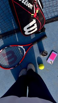 Tennis equipment on court with shadows, showcasing a racket, ball, and smartphone.