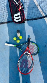 Tennis rackets and balls on a court under sunlight, ideal for sports themes.
