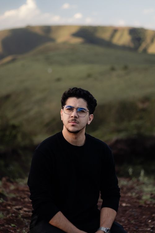 Free Portrait of a young man in a black sweater with scenic hills and cloudy sky. Stock Photo