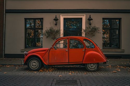 Free A classic red vintage car parked in front of a charming building surrounded by autumn leaves. Stock Photo