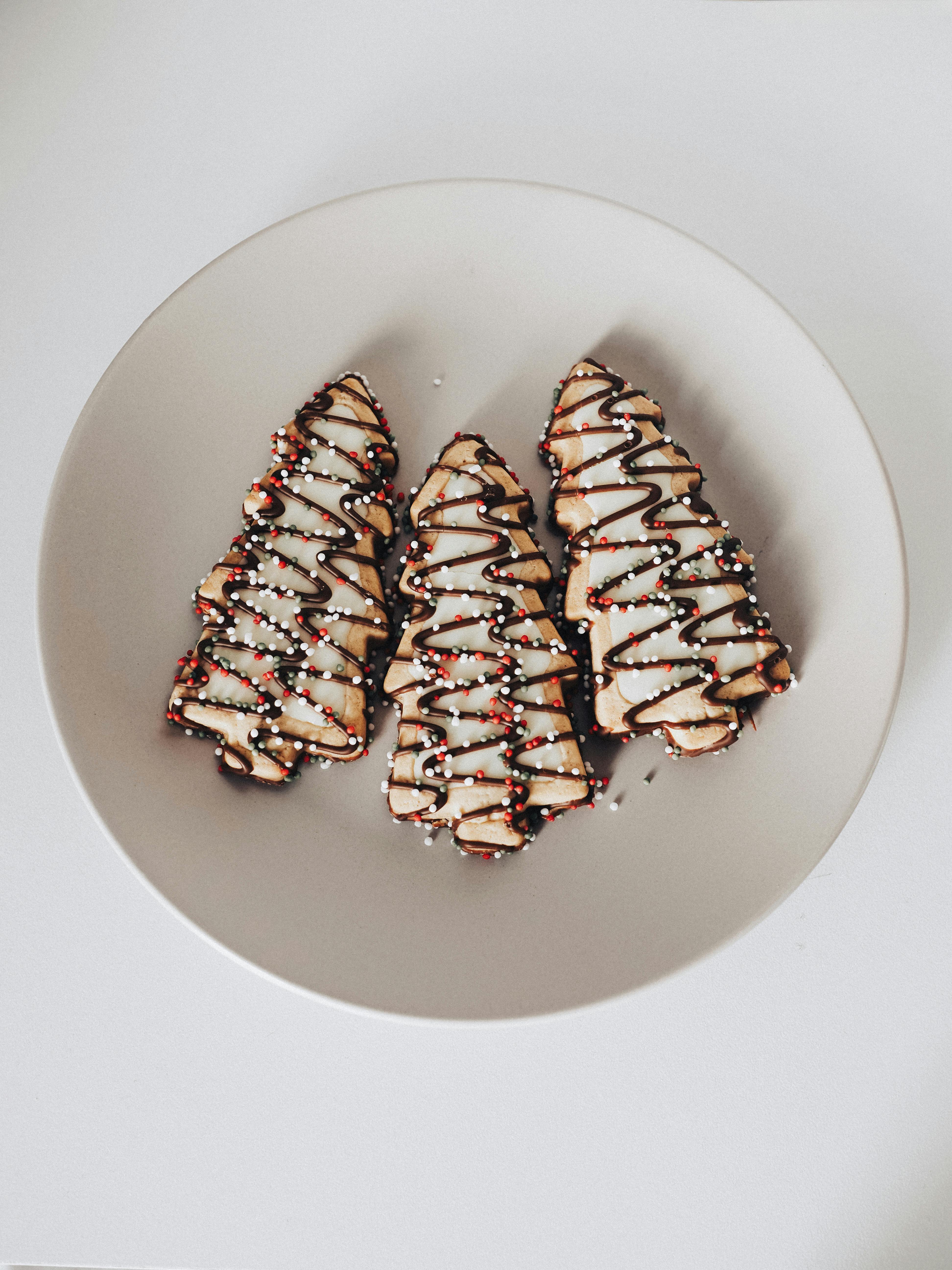 Delicious holiday cookies shaped as trees with icing and sprinkles on a plate.