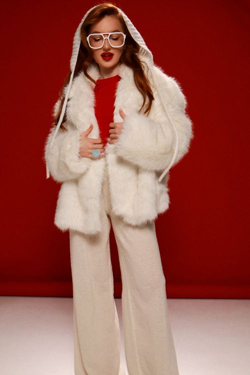 Free Fashionable woman in white fur coat and red top with bold glasses against red backdrop. Stock Photo