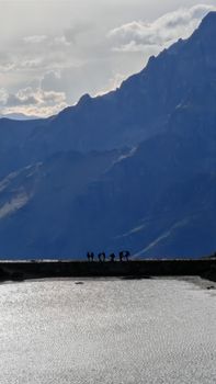Silhouetted figures near a reservoir with majestic Andean mountains in the background during daylight.