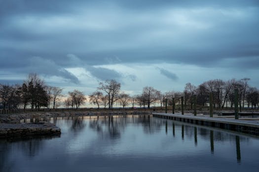 Tranquil lakeside view during winter with dramatic cloud formations reflecting on water at sunset.