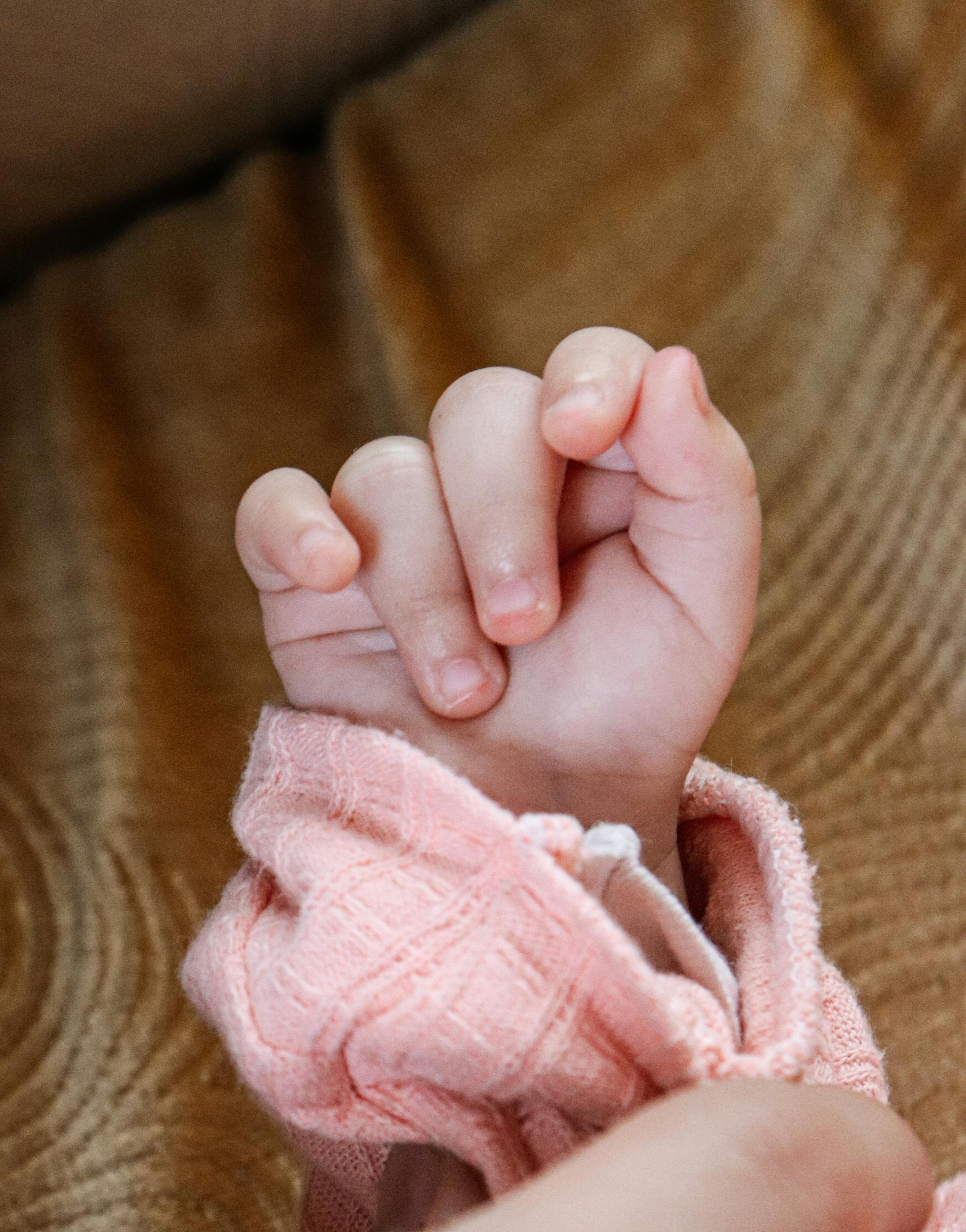Detailed close-up of a newborn's hand resting on a soft surface with a pink sleeve.