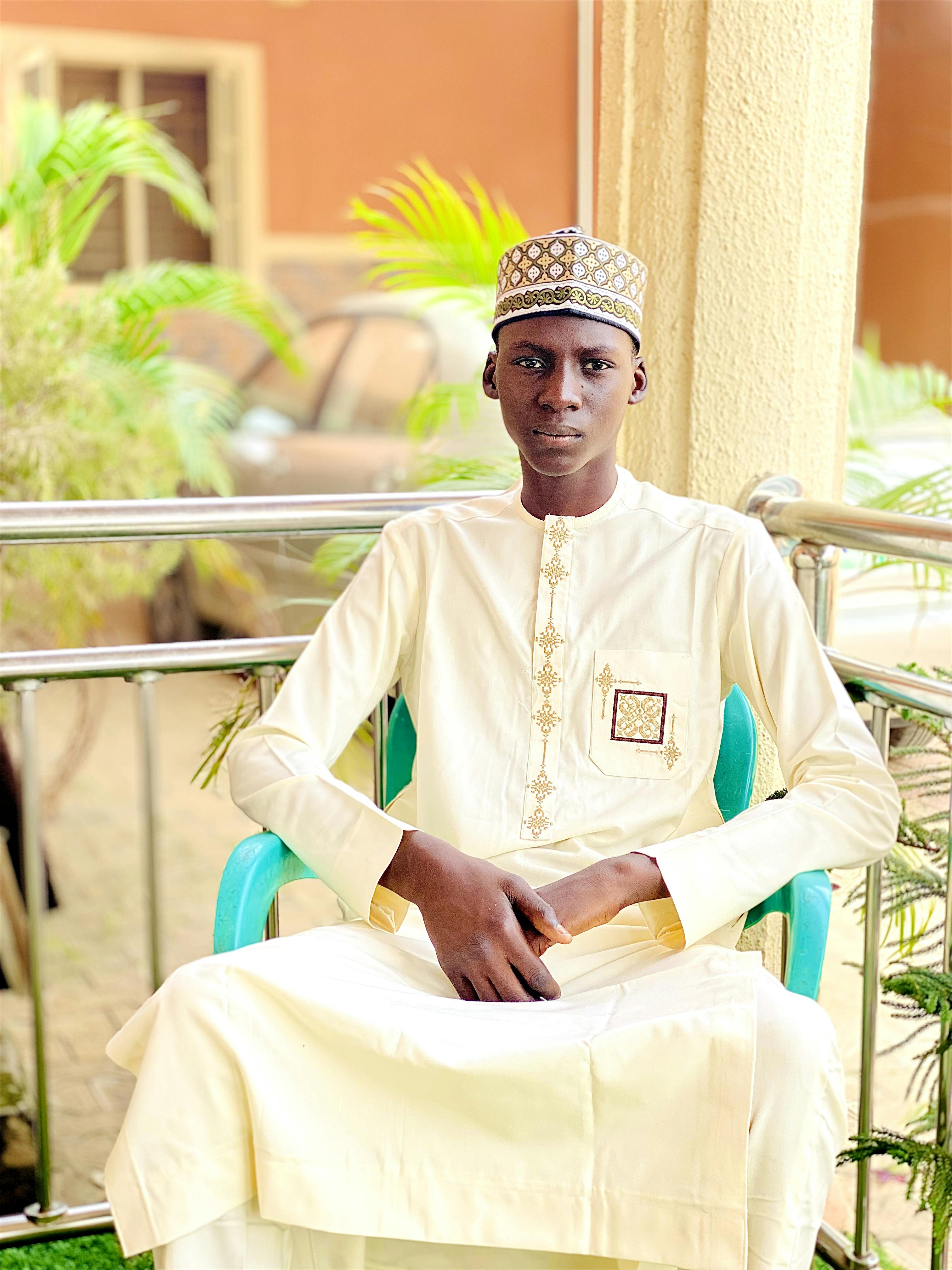 Portrait of a young man wearing traditional attire, seated outdoors on a sunny day.