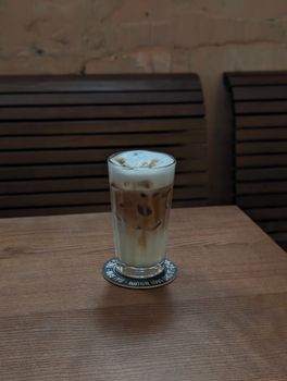 A chilled iced latte with milk froth served on a wooden table in a cozy cafe.