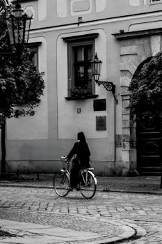 Elegant black and white photo of a cyclist on a historical street.
