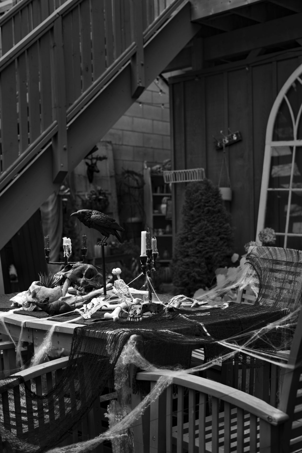 Black-and-white spooky outdoor Halloween table with skulls, a raven, cobwebs, and candelabras
