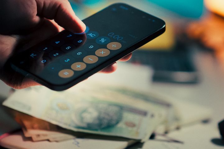 Celular, dinheiro e calculadora ilustrando a diferença entre saldo e valores comprometidos
