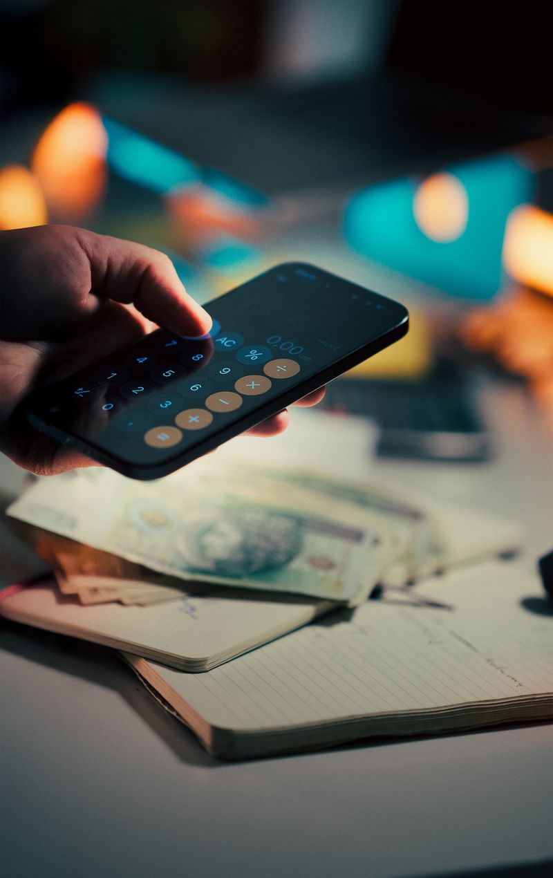手持智慧型手機使用計算器APP進行借款試算,旁邊放著現金與筆記本