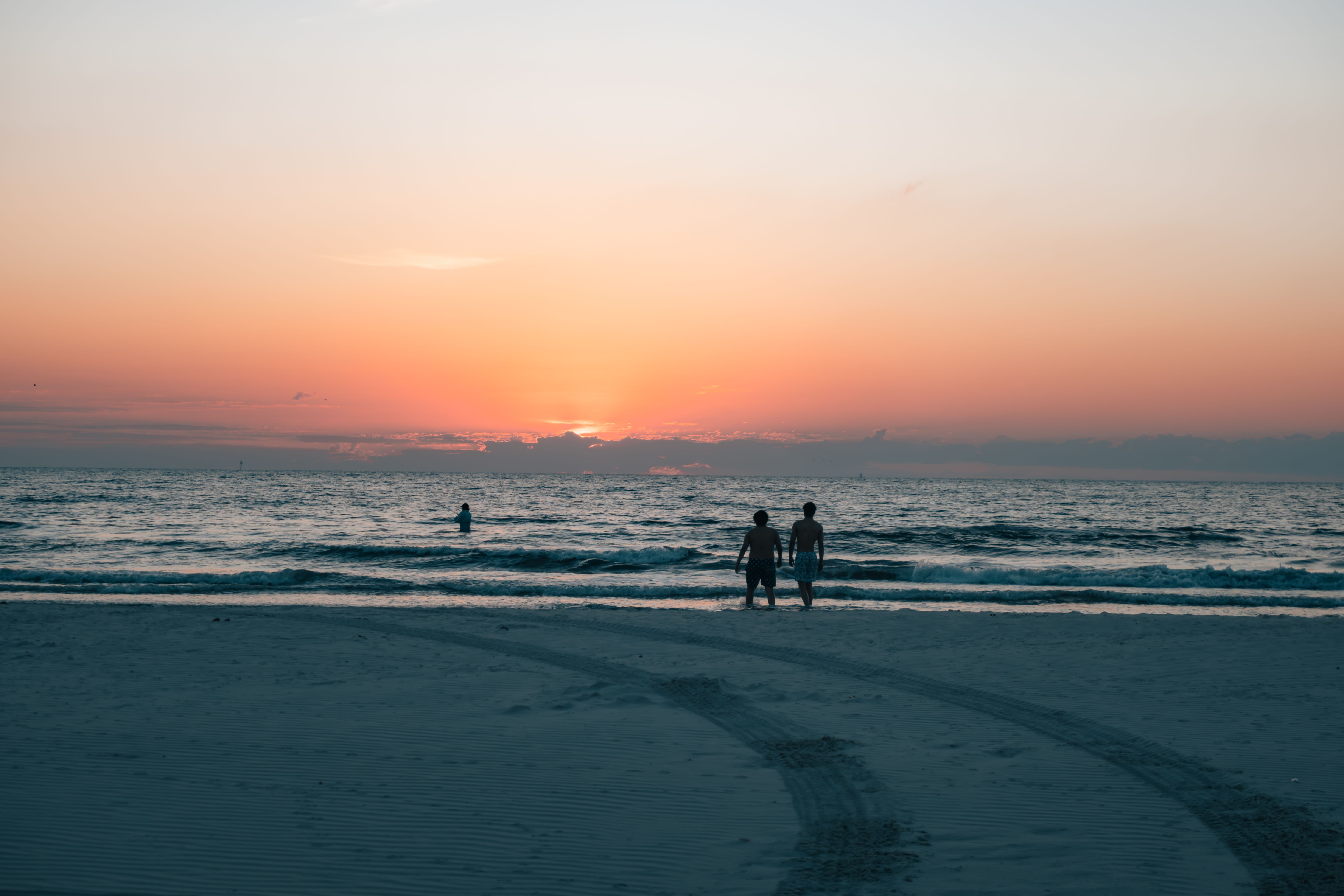 Gratis Fredfyldt solnedgangsscene på en strand med silhuetter mod den livlige horisont. Lagerfoto