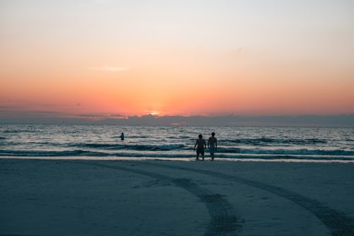 Free Peaceful sunset scene on a beach with silhouettes against the vibrant horizon. Stock Photo