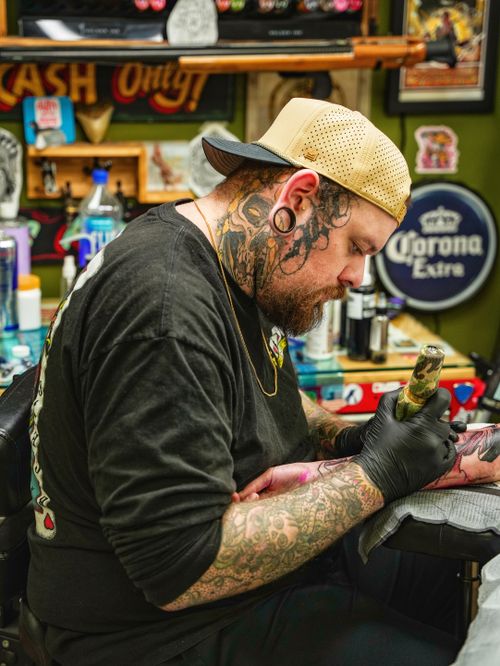 Free Tattoo artist focused on creating intricate designs in a vibrant shop setting with diverse artwork on walls. Stock Photo