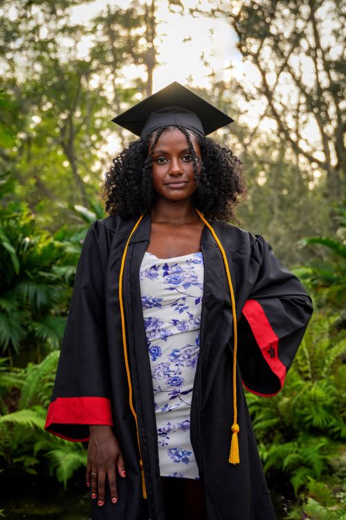 Free Young woman in graduation attire standing amid greenery, celebrating achievement. Stock Photo