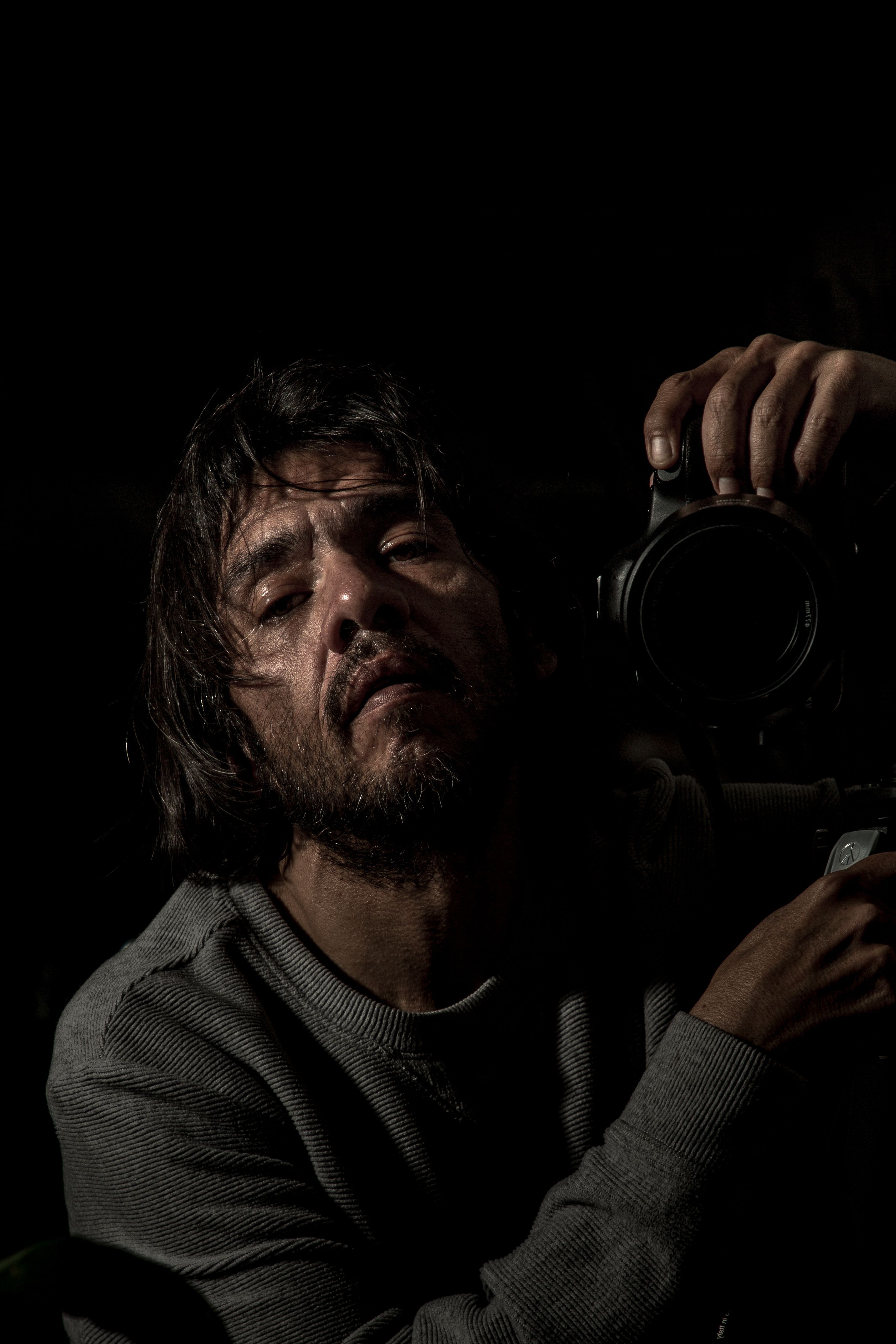 Dark and moody portrait of a photographer with camera, capturing introspection.