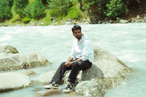 Free A man in casual attire sits on rocks by the Lidder River in Kashmir's scenic landscape. Stock Photo
