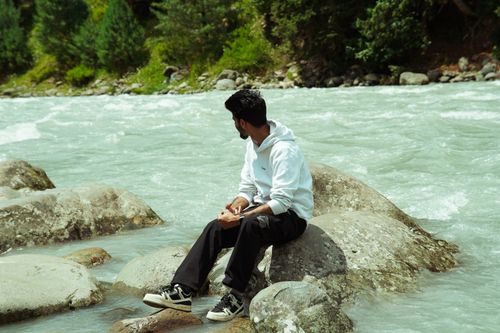 Free A man sits on rocks by the Lidder River in Pahalgam, enjoying the serene natural surroundings. Stock Photo