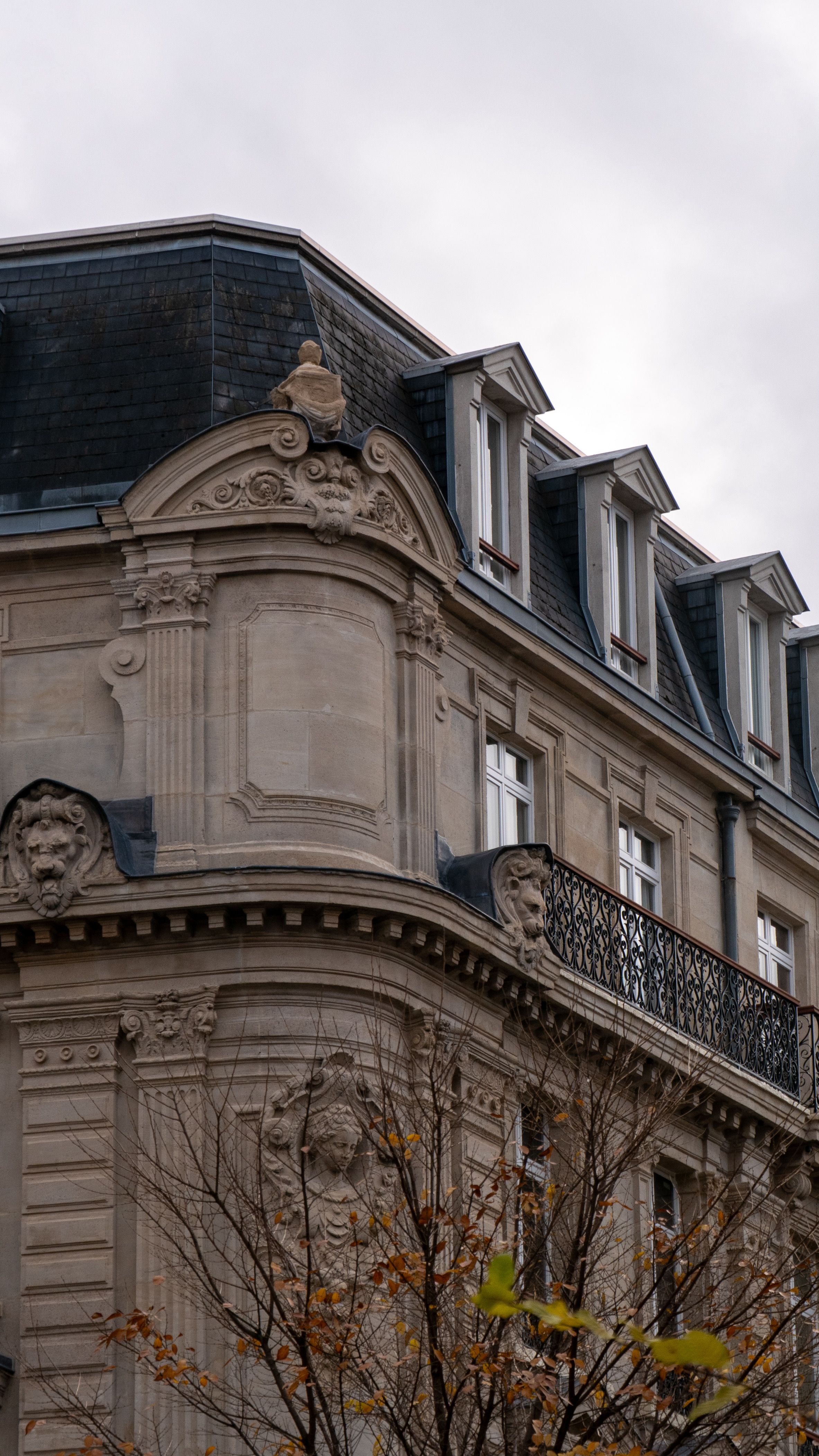 Détail architectural d’un immeuble parisien : corniche et modénature sous ciel gris.