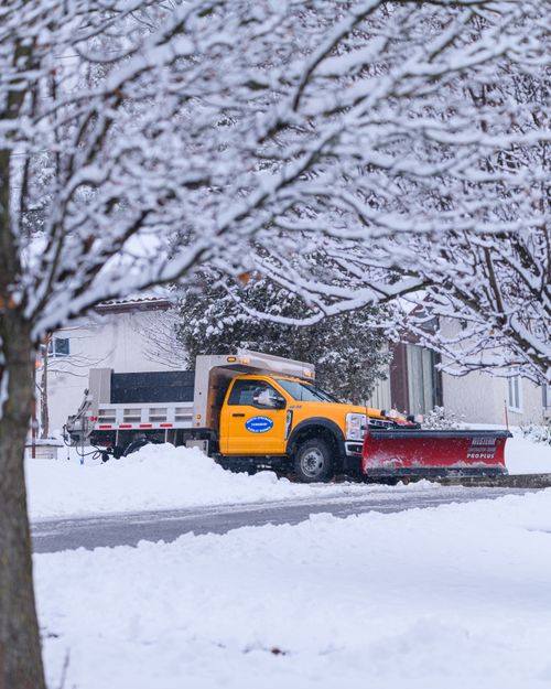 Free A yellow snowplow truck clears snow from a residential street in winter. Stock Photo