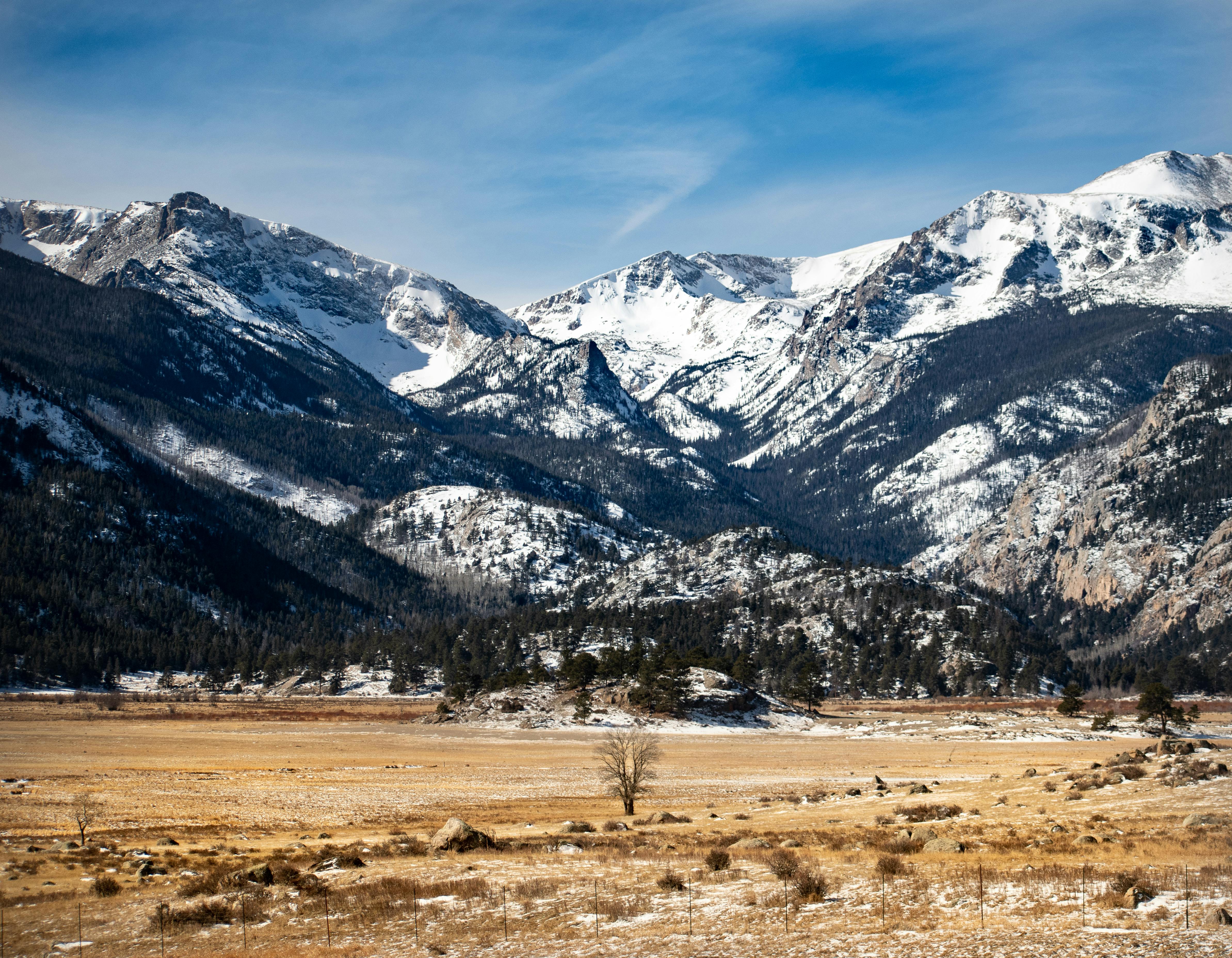 Expansive view of the Rocky Mountains with snow-covered peaks in Colorado under a clear blue sky.
