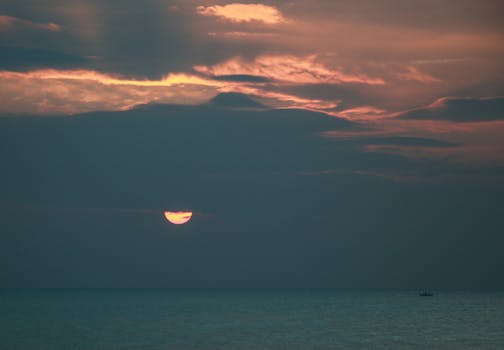 Dramatic sunrise over calm ocean with vibrant sky and small boat on the horizon.